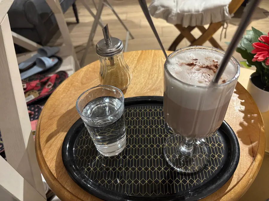 Latte im Glas mit Zimt und ein Glas Wasser auf schwarzem Tablett