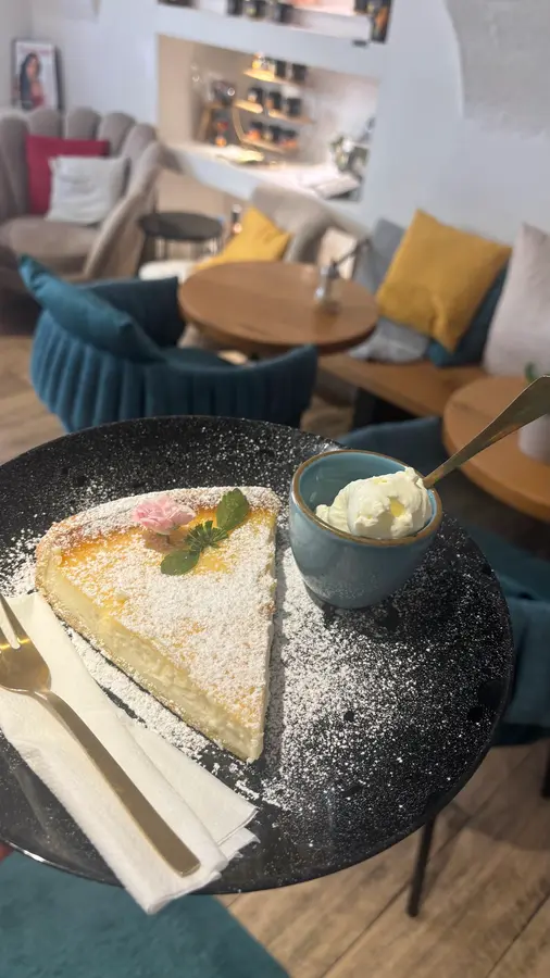Stück Kuchen mit Staubzucker und einer kleinen Schale, dahinter Sessel in Petrol