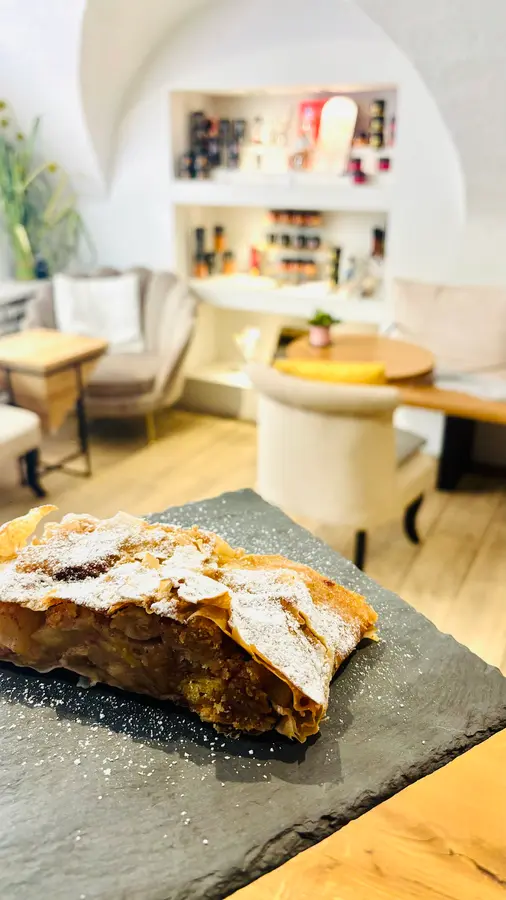 Strudel mit Staubzucker auf einer Schieferplatte, dahinter das helle Gewölbe mit Sesseln und Regalen
